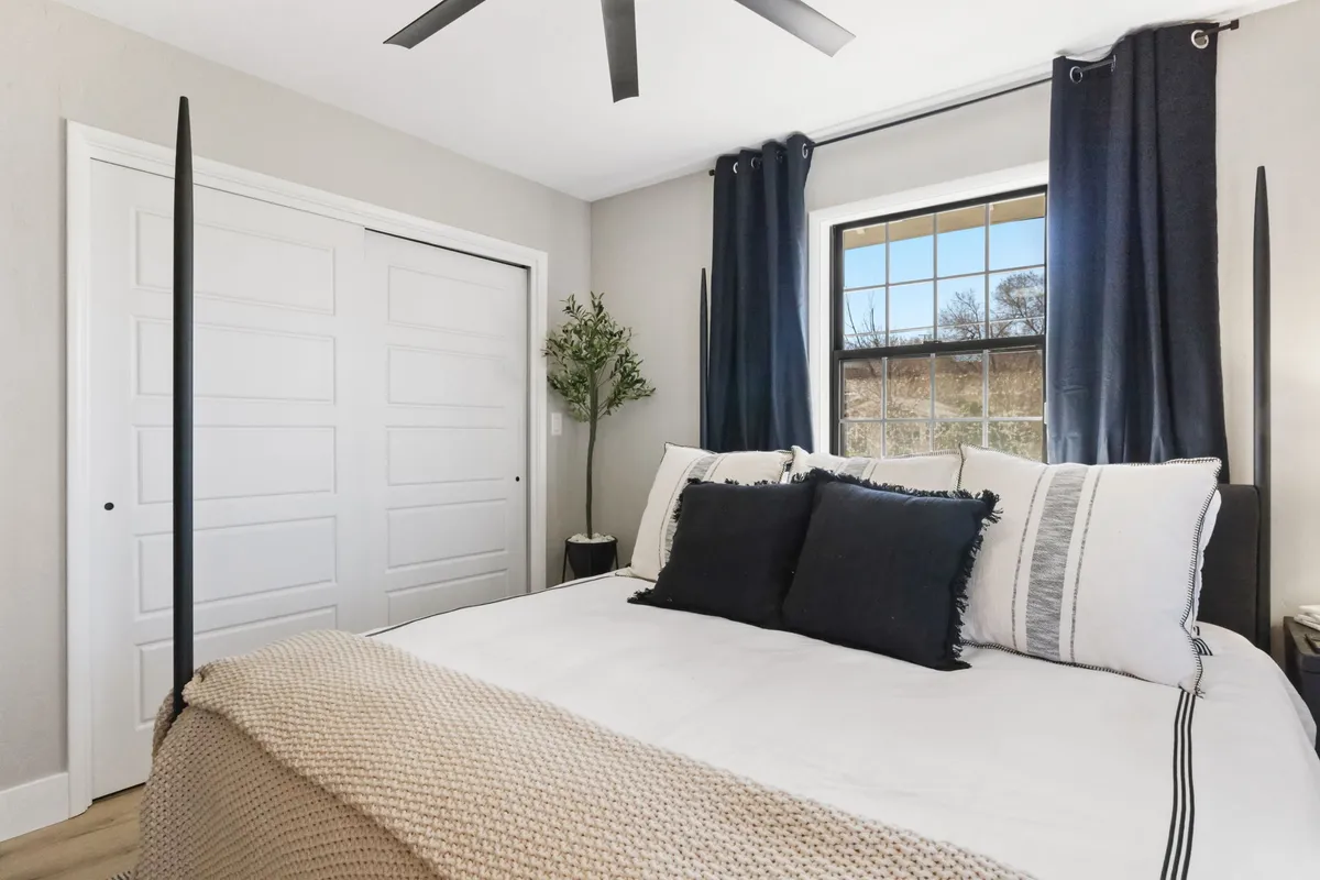 A relaxing bedroom scene with a comfortable bed, window with curtains allowing in gentle light, and a leafy plant. The space is calm and cozy, ideal for resting or enjoying a quiet morning with a book.