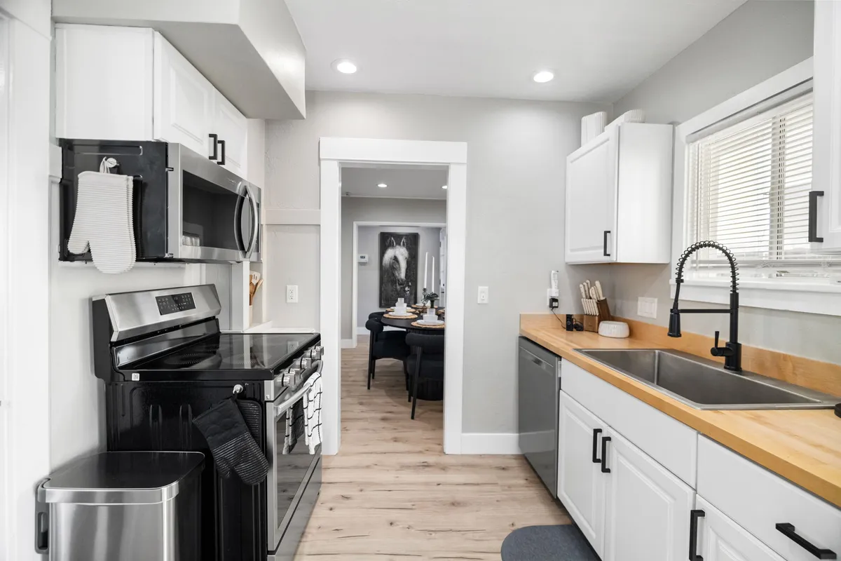 A contemporary kitchen showcasing stainless steel appliances, a wooden countertop, a sink, and a view into an adjacent dining or entertaining area. The space feels open and conducive to hosting or cooking with loved ones.