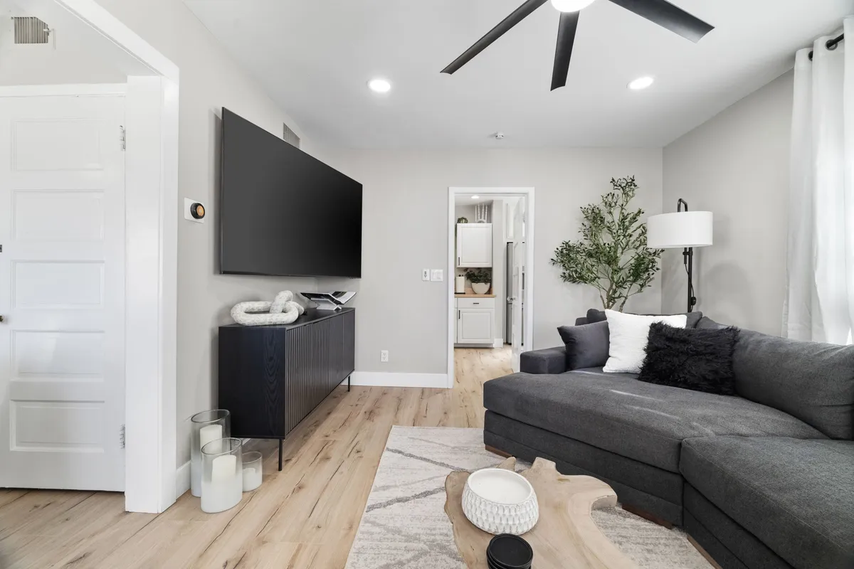 A cozy and contemporary living room featuring a plush sofa, a coffee table, decorative plant, and a TV. Sunlight filters in, highlighting the open space and comfortable seating arranged for conversation and relaxation.