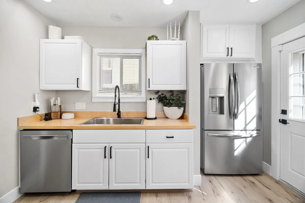 A bright, inviting kitchen scene featuring a stainless steel refrigerator, wooden countertops, and an open window allowing natural light to pour in. The setup is ideal for group cooking sessions or a casual breakfast shared at the counter, with ample space for several people to gather and interact.