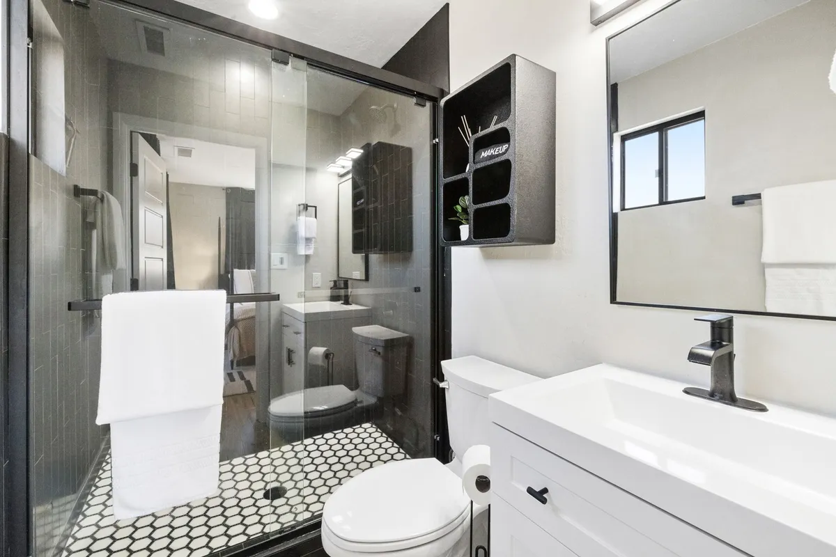 A contemporary bathroom scene with a glass shower enclosure, striking black and white tile flooring, a modern vanity, and wall-mounted storage. The space exudes a clean, peaceful vibe ideal for relaxation and personal care.