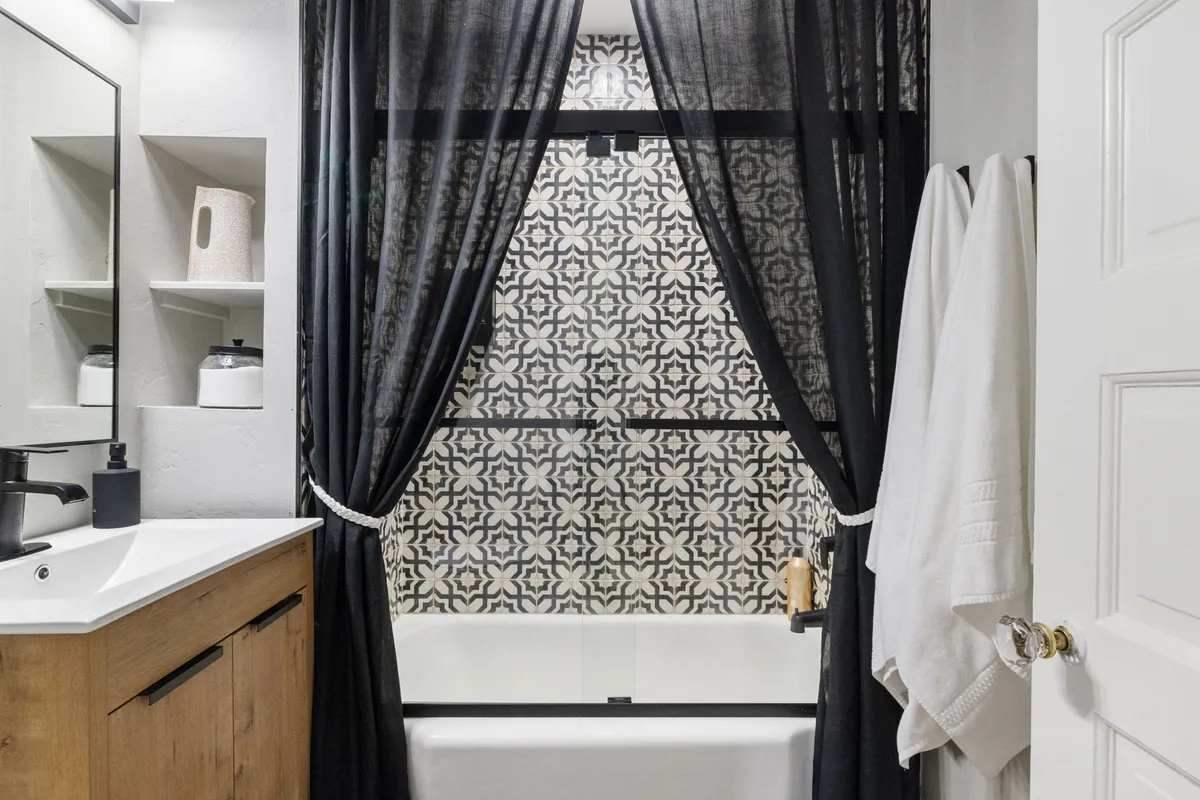 A tranquil bathroom featuring a bathtub with decorative tiles and curtains, suggesting a soothing place for bathing and self-care routines. The mood is calm and inviting, perfect for unwinding after an adventure-filled day.
