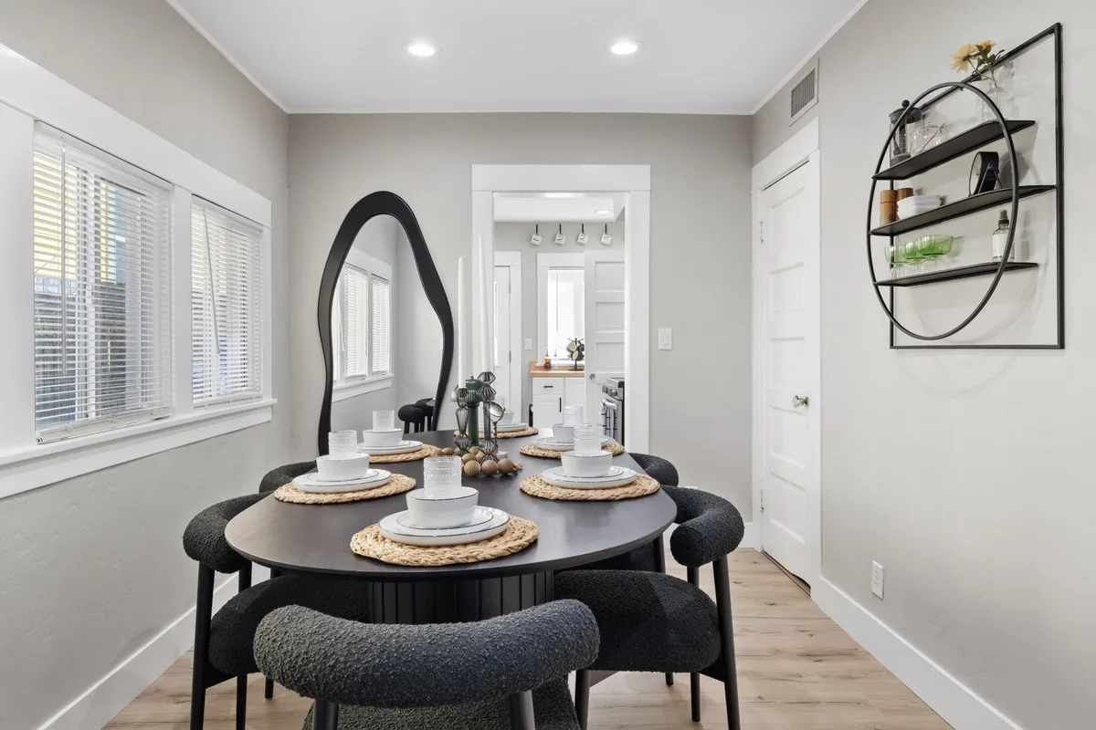 A cozy and stylish dining nook with a round dining table, modern chairs, a decorative wall shelf, and a large mirror reflecting light. The inviting setup hints at intimate meals or coffee moments in a contemporary setting.