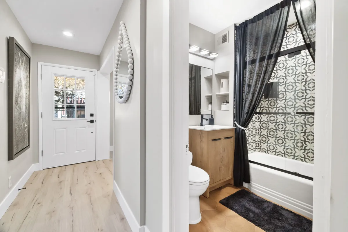 This image shows the front door area with a mirror, bathroom features visible nearby, and decorative art on the wall. The setting offers a sense of arrival and transition, hinting at the welcoming experience guests will have as they step into the property before heading out to explore downtown.